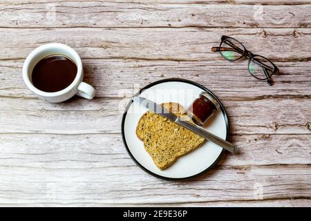 Toast und Marmelade auf einem Teller neben einem Kaffee Auf einem Holztisch, um die Frühstückszeit darzustellen Stockfoto
