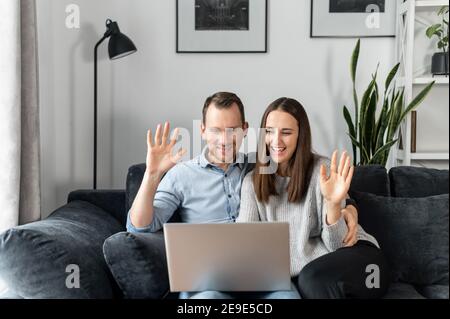 Ein Ehepaar verwendet Laptop für Video-Verbindung, eine Frau und Mann verzichten in Webcam mit fröhlichem Lächeln sitzen auf der bequemen Couch Stockfoto