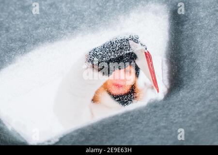 Frau im Winter, um das Auto von Schnee zu reinigen Ihr eigenes - sie bürstet die Windschutzscheibe mit Schnee bedeckt Stockfoto