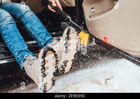 Frau putzt Schnee von den Stiefeln, bevor sie ins Auto kommt - Starker Schneefall im Winter Stockfoto