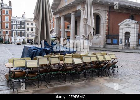 Gemäß den Einschränkungen der Regierung für die soziale Distanz von Covid werden Tische und Stühle eines geschlossenen Restaurantbetriebs "Laduree" während der dritten Sperre der Coronavirus-Pandemie am 3rd. Februar 2021 in London, England, auf der Covent Garden Piazza gestapelt und zusammengebunden. Stockfoto