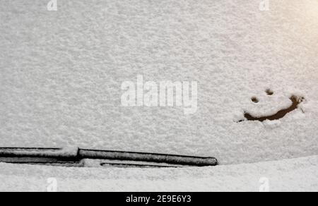 Schneehintergrund. Textur von nassem Schnee mit einem fröhlichen Smiley-Symbolmuster im Winterfenster des Autos im Nahbereich. Lächeln Sie im Schnee, glücklich Stockfoto