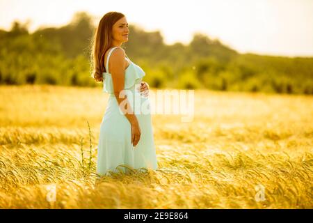 Ziemlich junge schwangere Frau in weißen Kleid entspannend draußen in Natur am Sommertag Stockfoto