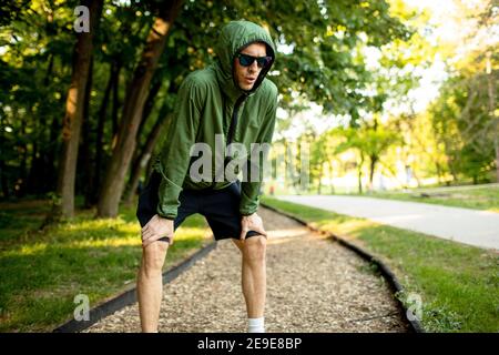 Schöner, athletischer junger Mann, der eine Pause beim Training macht Im sonnigen grünen Park Stockfoto