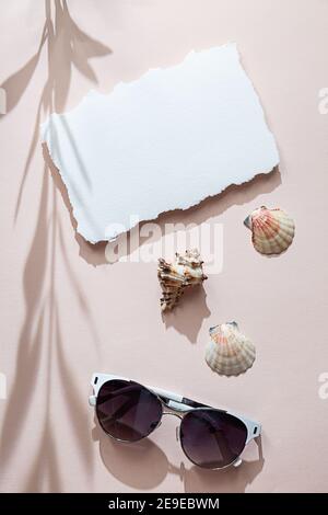 Sommerstillleben mit weißem Blatt Papier, Muscheln, Sonnenbrillen, langen Schatten eines Olivenzweiges auf einem weichen rosa Hintergrund. Moderne Postkarte, Mock U Stockfoto