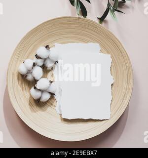 Sommer Stillleben Szene mit einem Olivenzweig und Schatten auf einem zarten rosa Hintergrund. Ein leeres Blatt Papier mit Baumwollblumen liegt auf einem Bambuspl Stockfoto