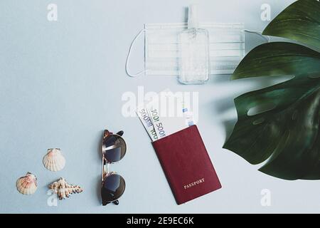 Stillleben Szene des Reisens in einer neuen Realität. Pass mit Geld, medizinische Gesichtsmaske und Handdesinfektionsmittel, Sonnenbrille, Muscheln und Monstera Palmblatt. Stockfoto