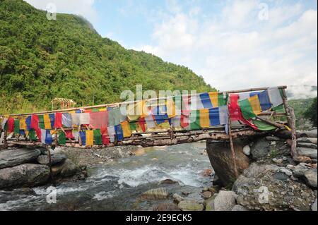 Tibetische Gebetsfahnen hängen an beiden Seiten eines verwitterten Holzbrücke über den Fluss Stockfoto