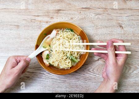 Hand halten Essstäbchen Kommissionierung chinesische gelbe Eiernudeln Topping Scheibe Gegrilltes Schweinefleisch mit roter Sauce in Suppe auf Schüssel zu Essen Stockfoto