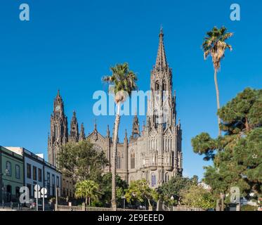 Blick auf die wunderschöne Pfarrkirche San Juan Bautista, beeindruckende neogotische Kathedrale in Arucas, Gran Canaria, Spanien. Blauer Himmel und Palmen Stockfoto