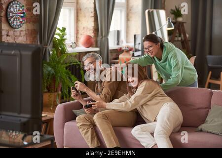 Glückliche Familie von drei sitzen auf dem Sofa und Spaß haben Während ihrer Wiedergabe in Videospiel Stockfoto