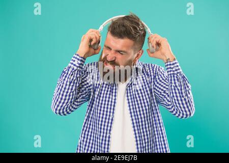kaukasischer Kerl mit Bart und Schnurrbart nicht wie laute Musik in digitalen Kopfhörern auf blauem Hintergrund, moderne Technologie. Stockfoto
