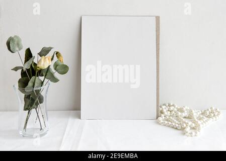 Mode Hochzeit Schreibwaren Mockup Szene. Eine leere vertikale Grußkarte und getrocknete weiße Blumen auf weißem Leinenhintergrund. Feminines Stillleben, top Stockfoto