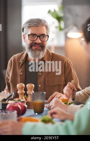 Reifer bärtiger Mann, der beim Mittagessen am Esstisch sitzt Seine Familie Stockfoto