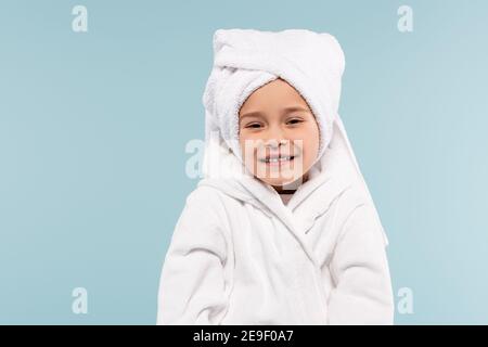 Glückliches Kind im Bademantel eingewickelt in Handtuch lächelnd isoliert auf Blau Stockfoto