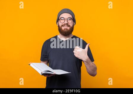 Bärtiger Hipster-Mann, der die Agenda des Planers hält und den Daumen nach oben zeigt. Stockfoto