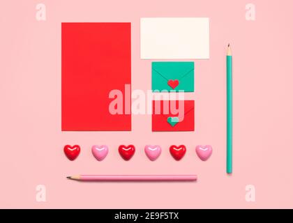 Alles Liebe zum Valentinstag.Papierumschläge mit roter Karte und rosa und Grüne Bleistifte auf rosa Hintergrund Stockfoto