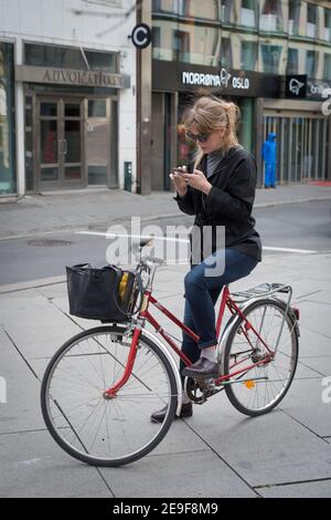 Eine junge Frau überprüft ihr Handy, während sie in Akersgata, Oslo, Norwegen, auf einem Fahrrad saß. Stockfoto