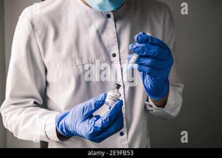 Nahaufnahme Arzt trägt blaue Handschuhe zieht die Covid-19-Impfstoff in eine Spritze, Vorbereitung für die Impfung Schuss. Stockfoto