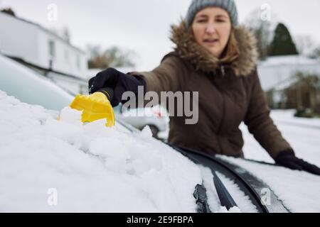 Frau Im Winter Clearing Schnee Von Windschutzscheibe Des Autos Mit Abstreifer Stockfoto