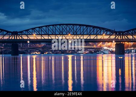 Personenzug, der über die Eisenbahnbrücke gegen die Stadt fährt. Stadtbild von Prag bei Nacht, Tschechische Republik Stockfoto