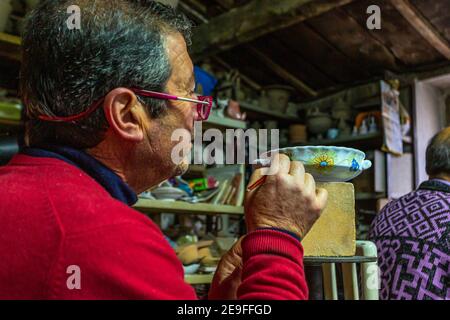 Mann, der in seinem Töpferatelier auf einem Tonkrug malt. Keramikmalerei Stockfoto