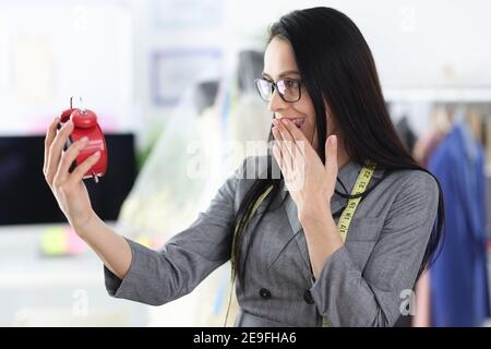 Frau Näherin schaut überrascht auf roten Wecker Stockfoto