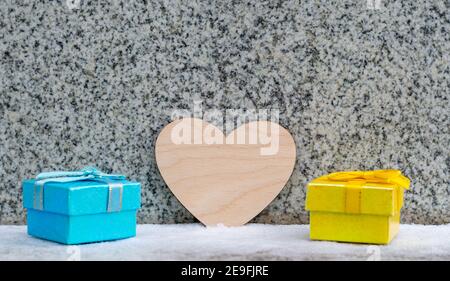 Valentinstag, Holzherz und zwei farbige Geschenkboxen stehen auf dem Schnee vor dem Hintergrund Stockfoto