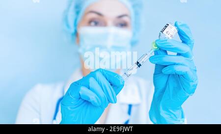 COVID-19 Coronavirus-Impfkonzept. Eine Ärztin in einer Maske hält eine Spritze und eine Medikamentenflasche, während sie sich darauf vorbereitet, eine Injektion zu verabreichen. Arzt Stockfoto