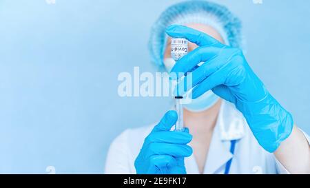 Hände der Ärztin mit Coronavirus-Impfstoff Nahaufnahme auf blauem Hintergrund Banner. COVID-19 Impfkonzept kreatives Banner. Der Arzt füllt eine syrin Stockfoto
