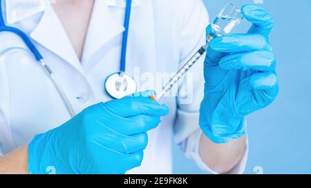 Ein Arzt mit einem Stethoskop in medizinischen Handschuhen füllt eine Spritze aus einem Fläschchen mit Medizin oder Impfstoff gegen Coronavirus. Vorbereitung auf Insulin i Stockfoto