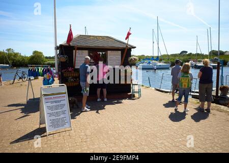 Foto von Leuten, die Schlange stehen für Bootstickets im Hafen von Christchurch, Devon, Großbritannien. Vor dem Ticketschalter befindet sich ein soziales Distanzschild. Stockfoto