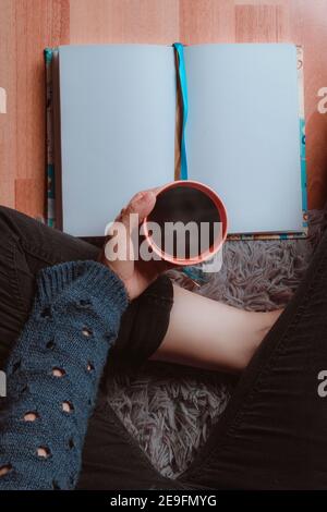 Nahaufnahme einer Frau, die eine Tasse heißen Kaffee trinkt, sehr komfortabel und ein Buch liest Stockfoto