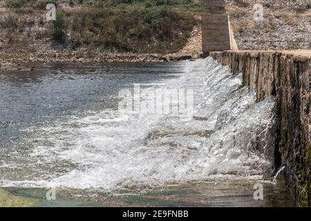 Der Wasserfluss führt das Wehr von der oberen Ebene nach der unteren Ebene den Seitenstrom des Flusses. Das Wehr bildet einen kleinen Wasserfall. Stockfoto