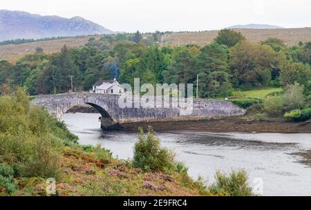 Rauch steigt aus einer ländlichen Hütte neben einem historischen Steinbrücke Stockfoto