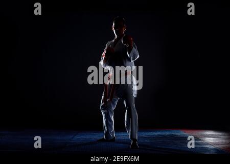 Mann in einem Kimono mit einen schwarzen Gürtel, nach vorn kicken auf schwarzem Hintergrund Stockfoto