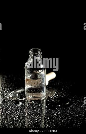 Glasflasche mit Medikamententropfer auf schwarzem und blauem Hintergrund mit Tropfen Flüssigkeit und Spritzern auf reflektierende Oberfläche. Medizinische Labortests. ICH Stockfoto
