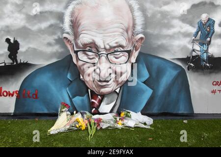 Blumen unter dem Wandbild von Sir Captain Tom Moore in Two Gates, Tamworth, nach der Ankündigung seines Todes von Covid. Stockfoto