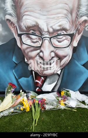 Blumen unter dem Wandbild von Sir Captain Tom Moore in Two Gates, Tamworth, nach der Ankündigung seines Todes von Covid. Stockfoto