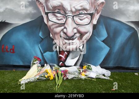 Blumen unter dem Wandbild von Sir Captain Tom Moore in Two Gates, Tamworth, nach der Ankündigung seines Todes von Covid. Stockfoto