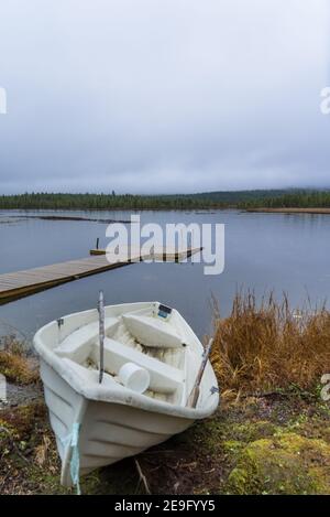 Altes, schmutziges, gebrautes Ruderboot, das neben einem kleinen Zielsee in Inari, Finnland, Lappland liegt. Hölzerner Pier an einem ruhigen und regnerischen Tag Stockfoto