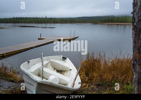 Altes, gebrautes Ruderboot liegt neben einem kleinen Zielsee in Inari, Finnland, Lappland. Hölzerner Pier im Cottage an einem entspannenden, ruhigen und regnerischen Tag Stockfoto