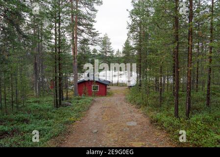 Weg zu einem schönen roten Holzhaus neben einem atemberaubenden See. Abgelegene einsame Hütte in Inari, Lappland, Finnland im grünen Kiefernwald. Autark Stockfoto