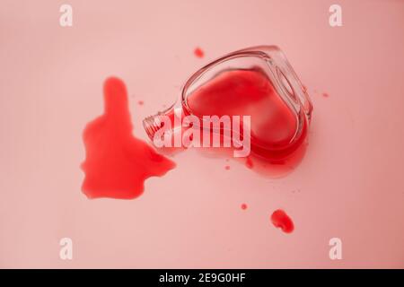 Herzförmige transparente Flasche gekippt auf einer rosa Oberfläche mit roter Flüssigkeit aus ihm, Zetinalansicht Stockfoto