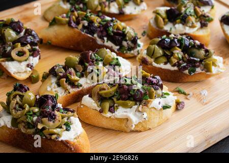 Herbed Olive Tapenade mit Ziegenkäse Bruschetta: Vorspeise aus Olive Tapenade und Ziegenkäse auf geröstetem Ciabatta Brot verteilt Stockfoto