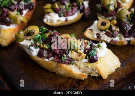 Herbed Olive Tapenade mit Ziegenkäse Bruschetta: Vorspeise aus Olive Tapenade und Ziegenkäse auf geröstetem Ciabatta Brot verteilt Stockfoto