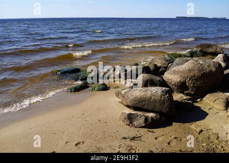 Die großen Steine am Strand des Rybinsker Stausees. Sommerseekape mit Wellenwasser und Melone. Jaroslawl Region, Russland Stockfoto