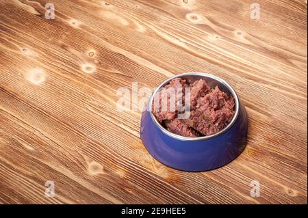 Dosenfutter für Katzen oder Hunde in einer blauen Metallschüssel auf einem Holzboden. Platz kopieren Stockfoto