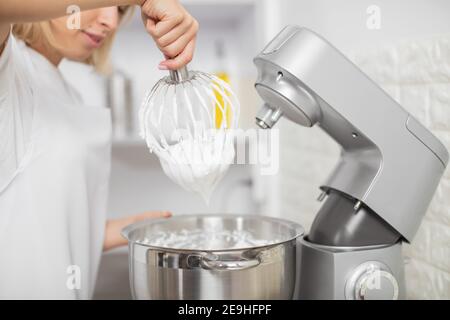 Nahaufnahme von einer professionellen Köchin, die in ihrer Konditorei Desserts zubereitet, Mischerschaufeln mit geschlagenem Eiweiß aus dem Essen neu zubereitet Stockfoto