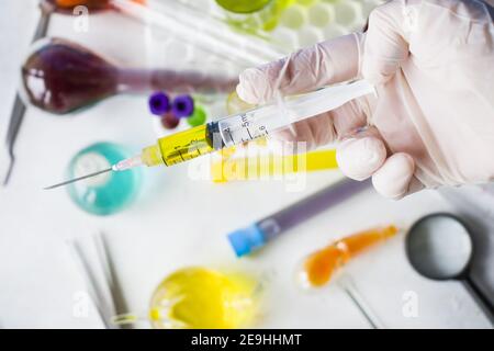 Selektiver Fokus einer Hand in Handschuhen, die eine Spritze halten Mit gelber Flüssigkeit auf unscharfem Hintergrund Stockfoto